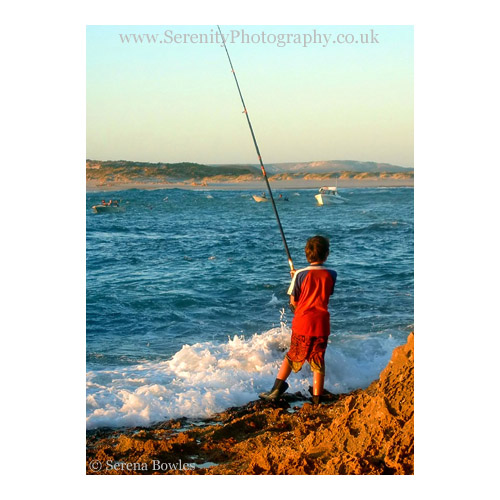 Small boy stands on the rocks fishing. Kalbarri, Australia.